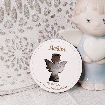 Etiqueta redonda branca com recorte de anjo e texto de batizado, junto a anjo em cerâmica azul