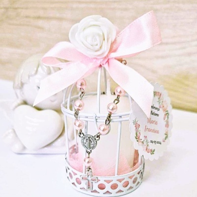 Castiçal branco decorativo com vela rosa, terço rosa e crucifixo, laço e flor brancos, etiqueta com nome e data