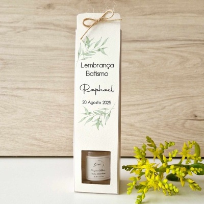 Caixa branca para lembrança de batismo com texto e ilustração de folhagem, e flores amarelas ao lado.