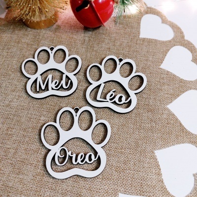 Ornamentos de madeira em forma de pata com nomes Mel, Léo e Oreo sobre tecido de juta