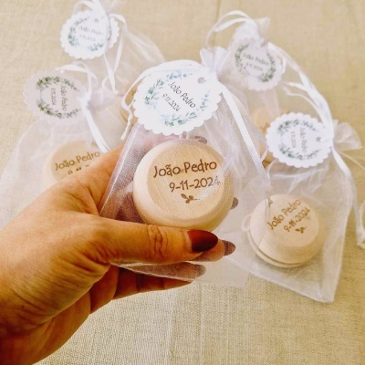 Caixas redondas de madeira claras com tampa em sacos de organza branco, etiquetas redondas com texto João Pedro 9-11-2024.