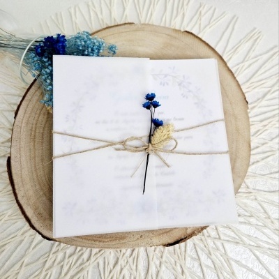 Convite branco com flores secas e fio rústico sobre base de madeira clara