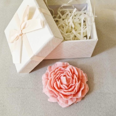 Caixa de presente branca aberta com vela rosa em forma de flor ao lado