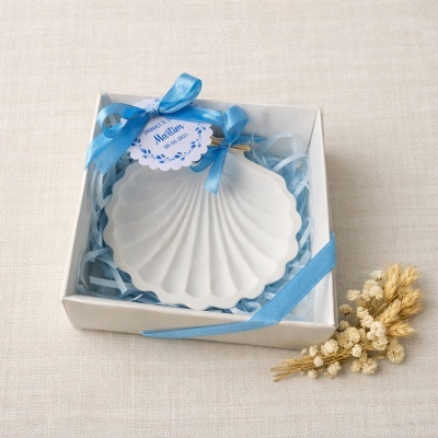 Prato decorativo em forma de concha branco numa caixa com fita azul e flores secas ao lado