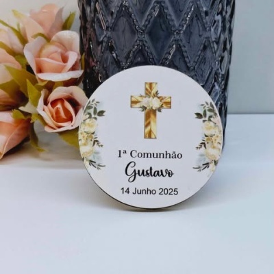 Etiqueta de primeira comunhão com cruz dourada e flores ao lado de vaso de vidro cinza e flores rosas