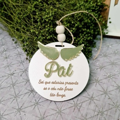 Disco decorativo branco com asas verdes e texto em relevo, pendurado com cordão de contas de madeira