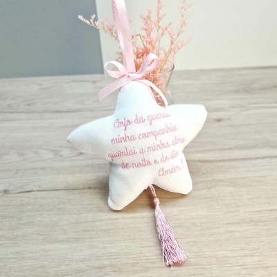 Almofada estrela branca com bordado rosa e fita, sobre mesa de madeira com vaso e flores secas cor-de-rosa