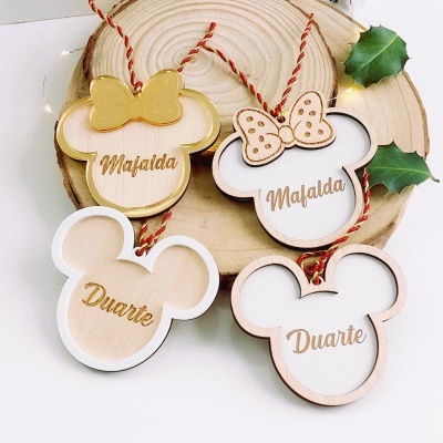 Decorações em forma de cabeça de rato de madeira com nomes Mafalda e Duarte, sobre placa de madeira redonda com folhagens e luzes.