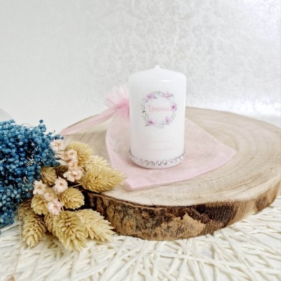 Vela branca decorativa sobre base de madeira com flores secas ao lado