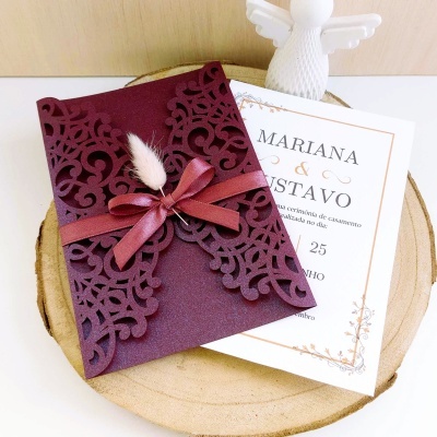 Convite de casamento bordô com padrão recortado, cartão branco com nomes e data, sobre base de madeira