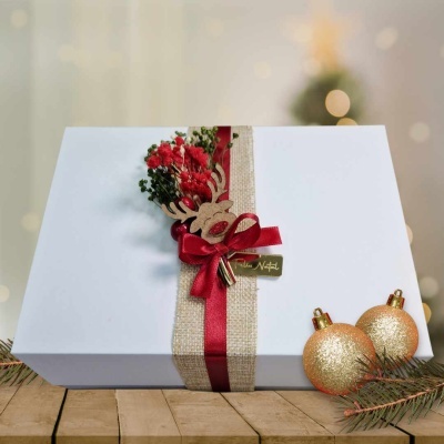 Caixa branca de presente com decoração natalícia em fita e flores, e duas bolas douradas brilhantes ao lado