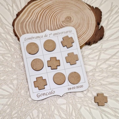 Jogo de peças de madeira redondas e em cruz sobre cartão branco comemorativo e base decorativa clara com padrão texturizado.