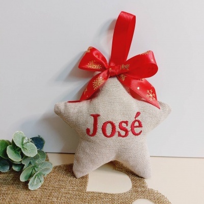 Ornamento estrela de tecido bege com nome José bordado a vermelho e fita vermelha de flocos de neve.