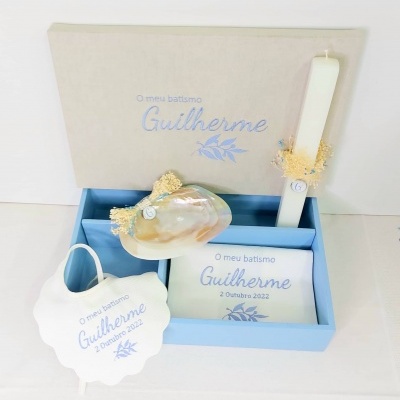 Conjunto para batismo com vela, toalha, concha e caixa decorada com texto em azul.