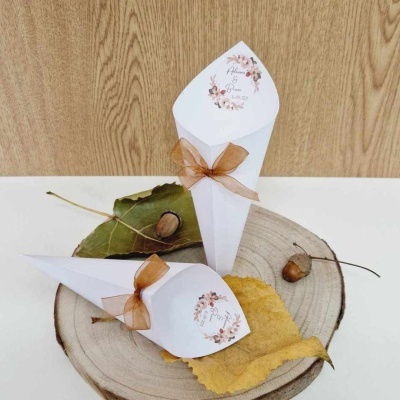 Dois cones de papel branco com laços castanhos sobre folhas e tábua de madeira