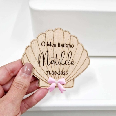 Peça em madeira em forma de concha com texto gravado e laço cor-de-rosa