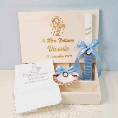 Conjunto de batismo com caixa de madeira, vela branca com fita azul, concha decorada, e toalha bordada.
