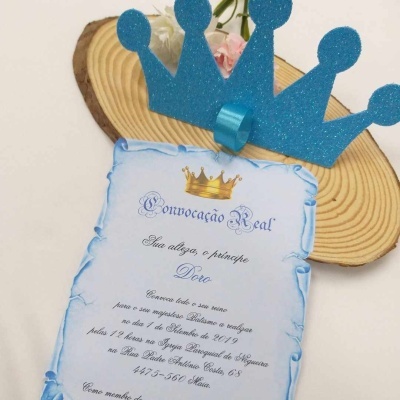 Convite de festa com texto 'Convocação Real' e coroa azul de papel com glitter em fundo branco e madeira