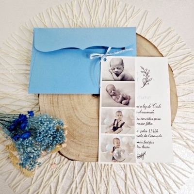 Convite de batizado com fotos de bebé, envelope azul e flores azuis sobre madeira