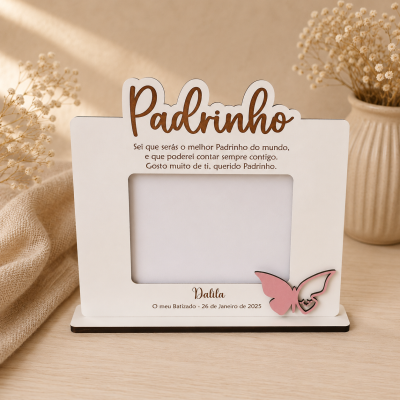 Porta-retrato branco com texto Padrinho em madeira castanha, borboleta rosa decorativa e texto gravado, sobre mesa clara com flores secas.