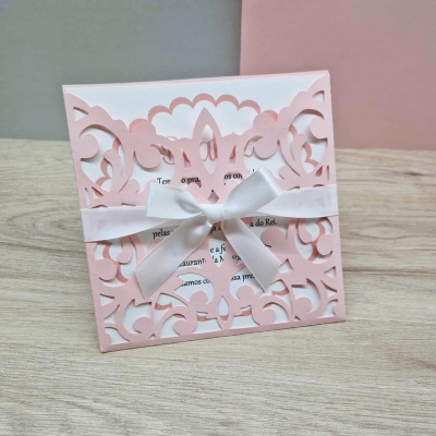 Convite rosa claro com recorte a laser e laço branco em superfície de madeira