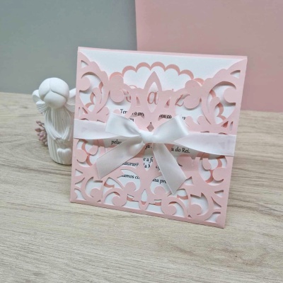 Convite cor-de-rosa com laço branco sobre superfície de madeira com estatueta branca ao lado