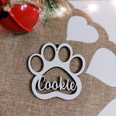 Ornamento em forma de pata com o nome 'Cookie' em branco sobre tecido de juta com sino vermelho e ramos de pinheiro