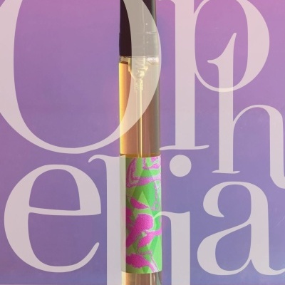 Perfume bottle with green and pink label on pink surface with purple background