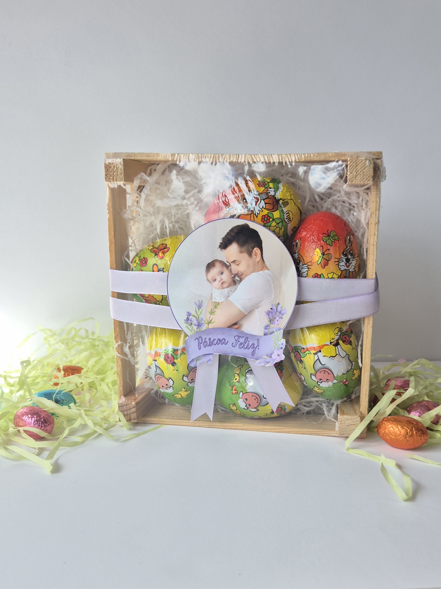 Caixa de madeira com ovos de Páscoa de chocolate coloridos e etiqueta com foto de homem e bebé