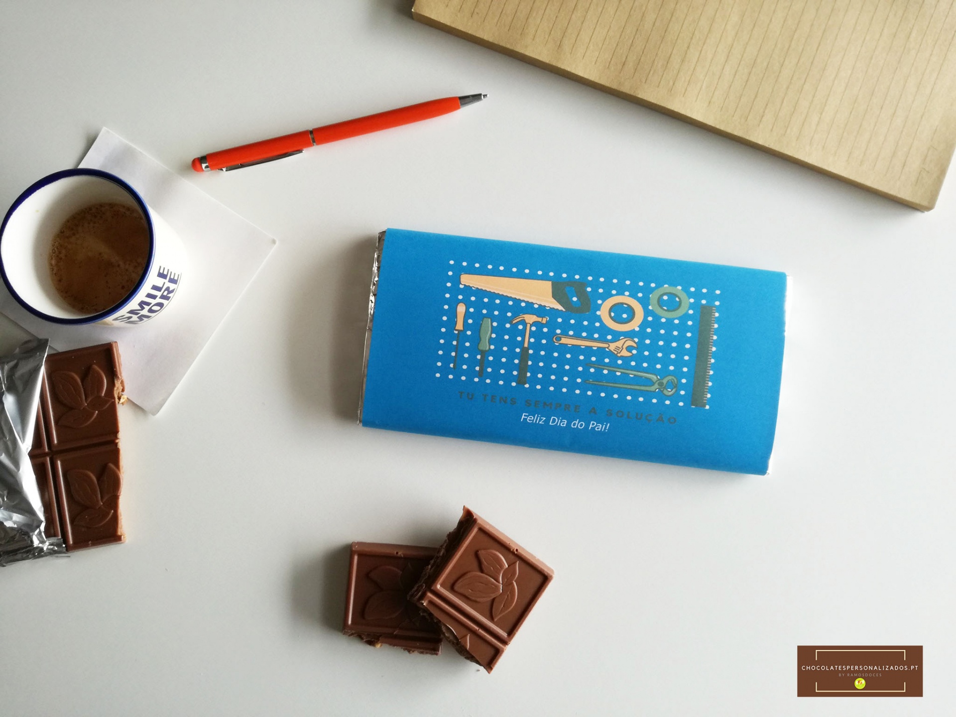 Barra de chocolate azul, pedaços de chocolate, caneca de café, caneta e caderno sobre superfície branca