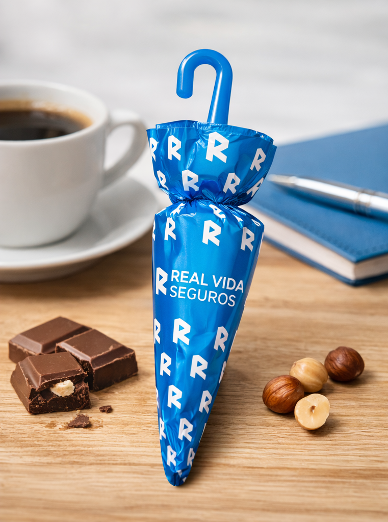 Embalagem azul com letras R e texto REAL VIDA SEGUROS junto a chocolate, avelãs, café e caderno numa mesa