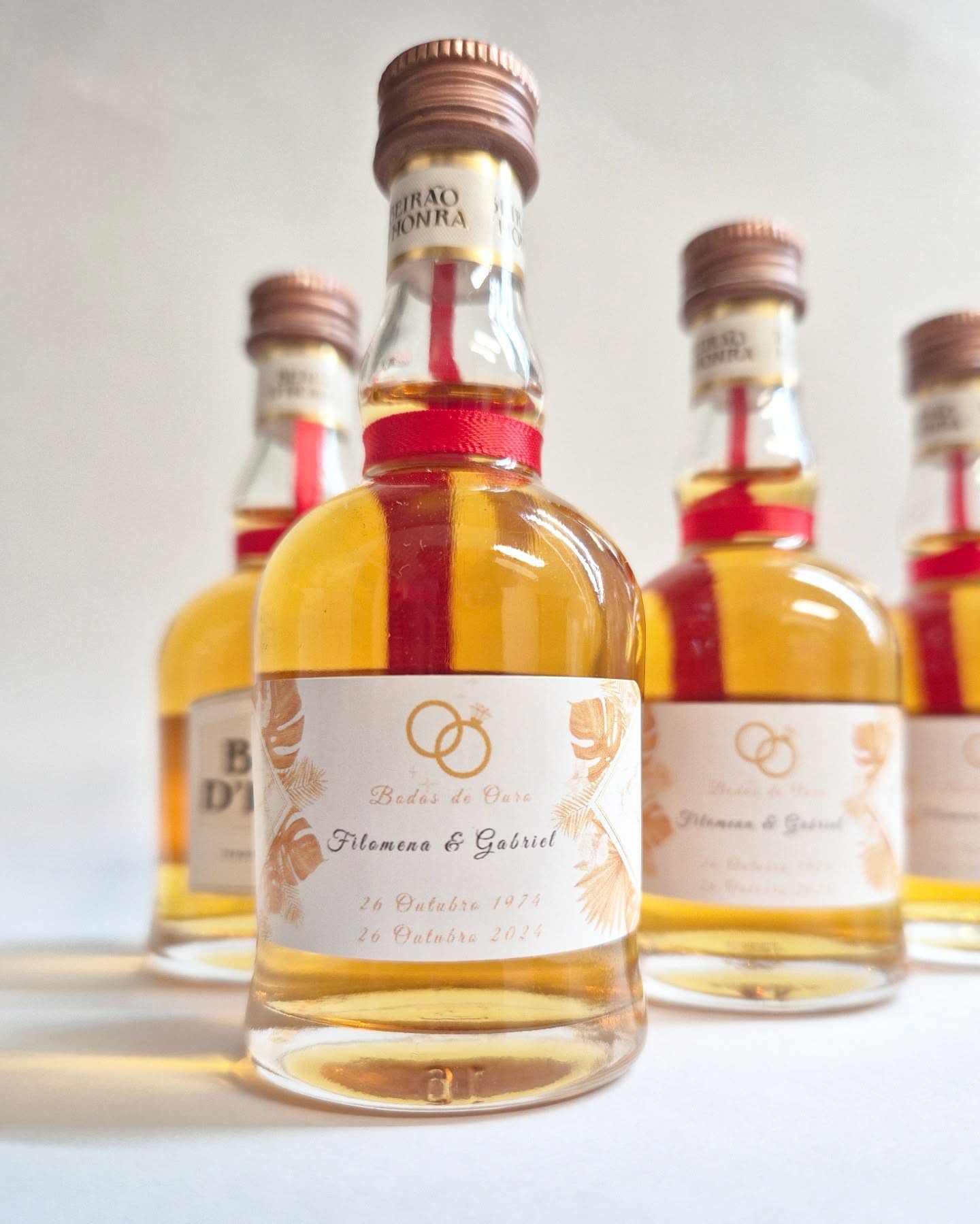 Garrafas pequenas de vidro com líquido amarelo e etiquetas de Bodas de Ouro