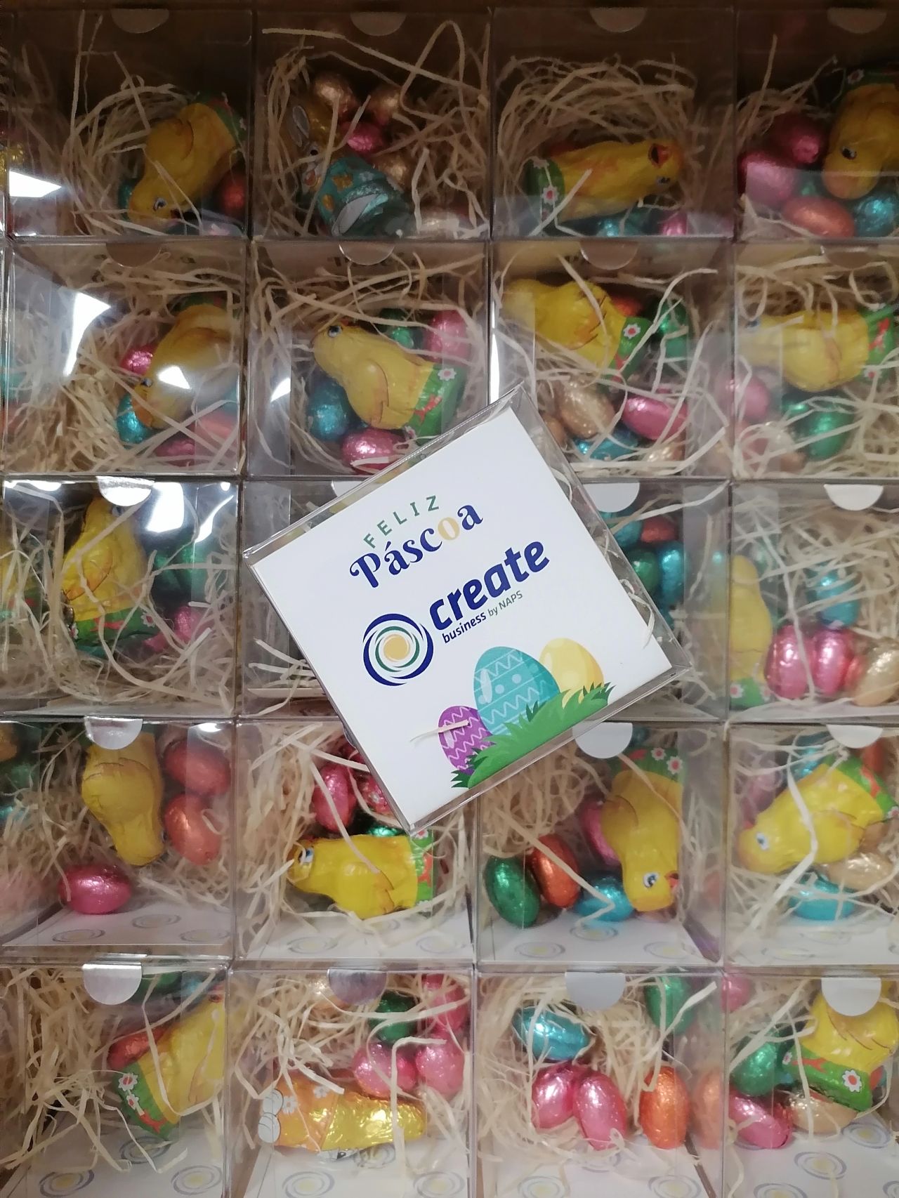 Caixas com chocolates em forma de pintainhos amarelos e ovos coloridos com cartão da Páscoa ao centro