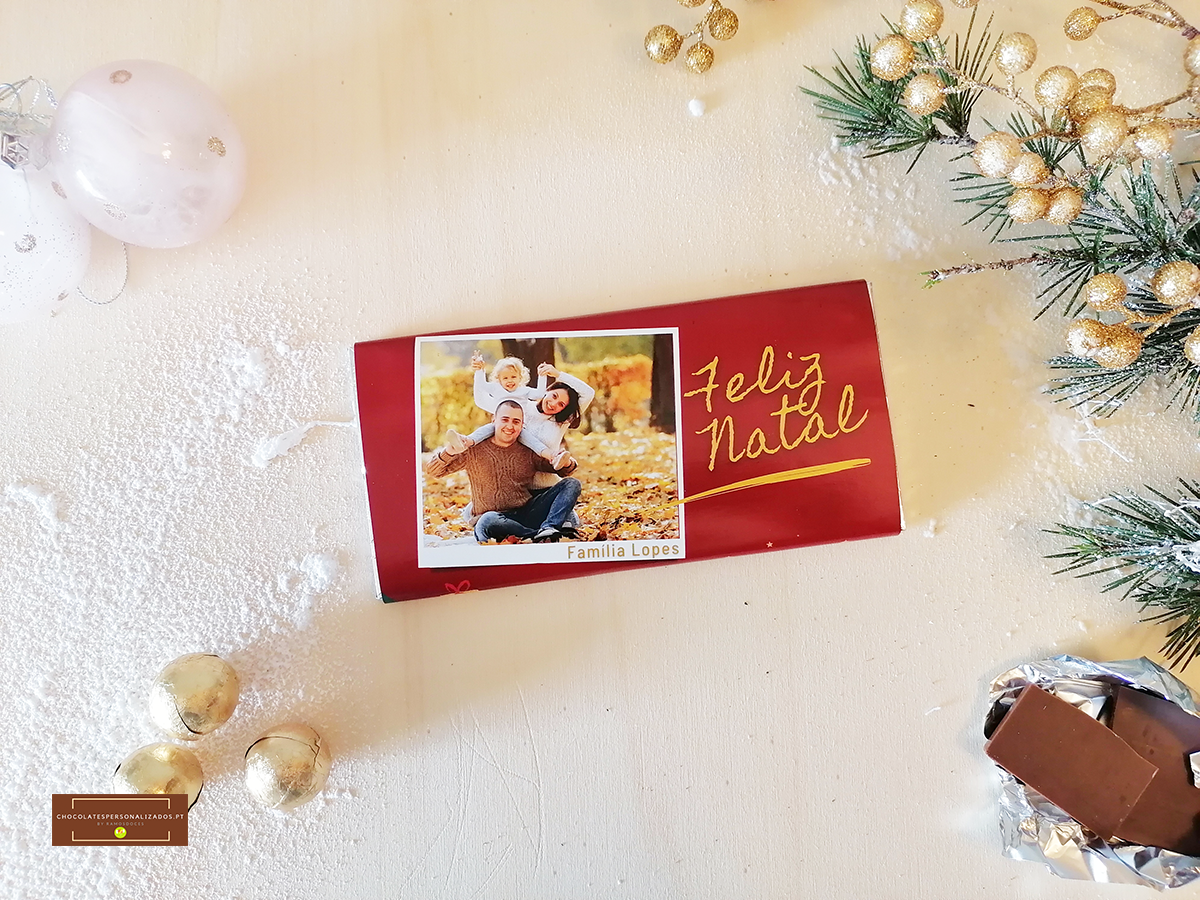 Embalagem vermelha com foto e texto 'Feliz Natal' e decoração natalícia em fundo claro