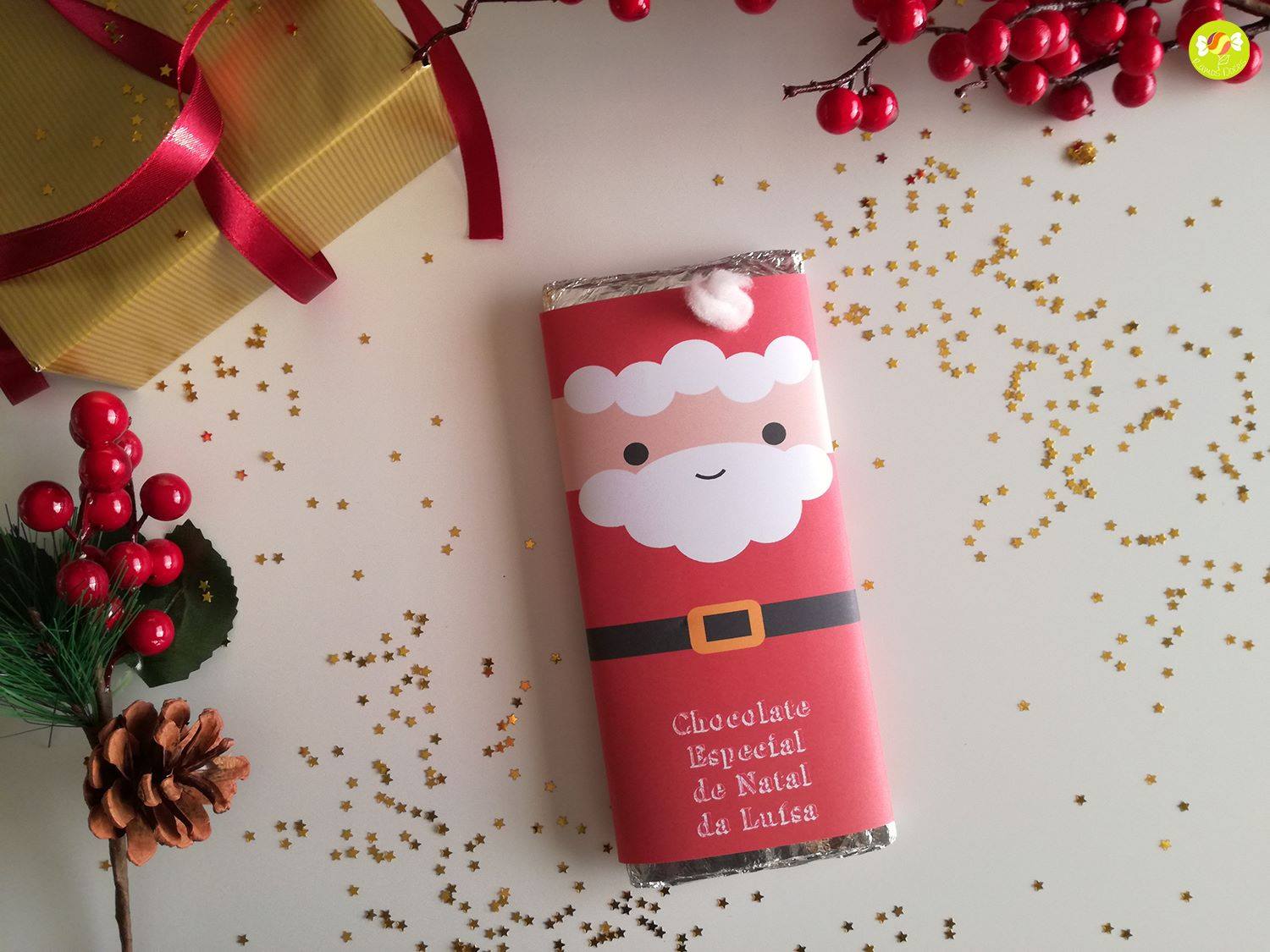 Barra de chocolate de Natal com embalagem vermelha decorada com Pai Natal e confetis dourados em superfície branca