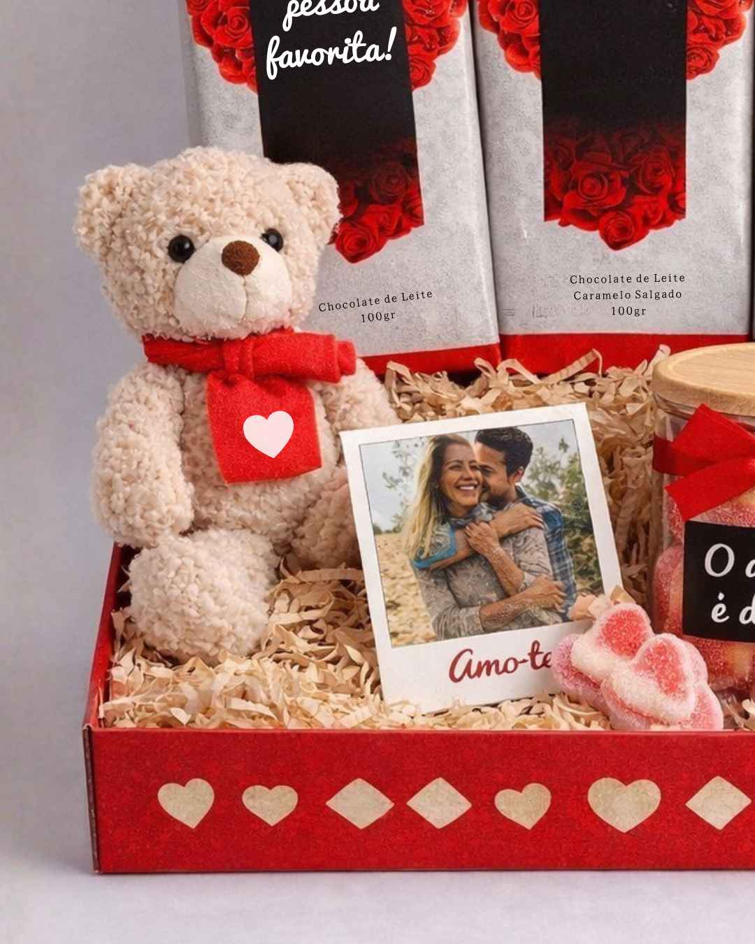 Caixa vermelha com urso de peluche, chocolates, frasco e cartão com foto de casal