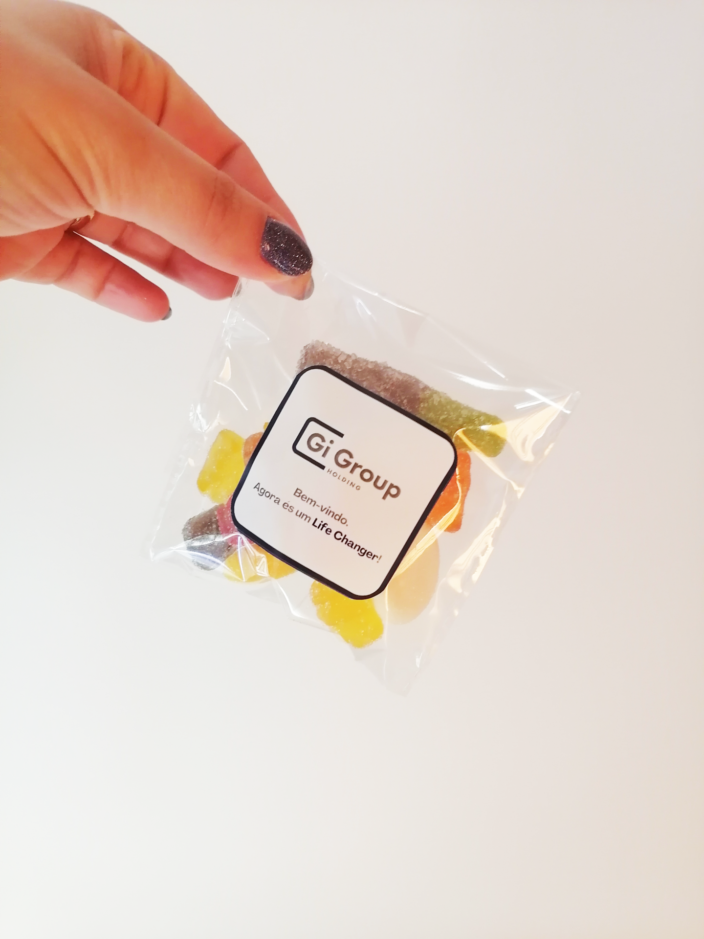 Mão segurando pacote transparente com balas coloridas e rótulo Gi Group Portugal