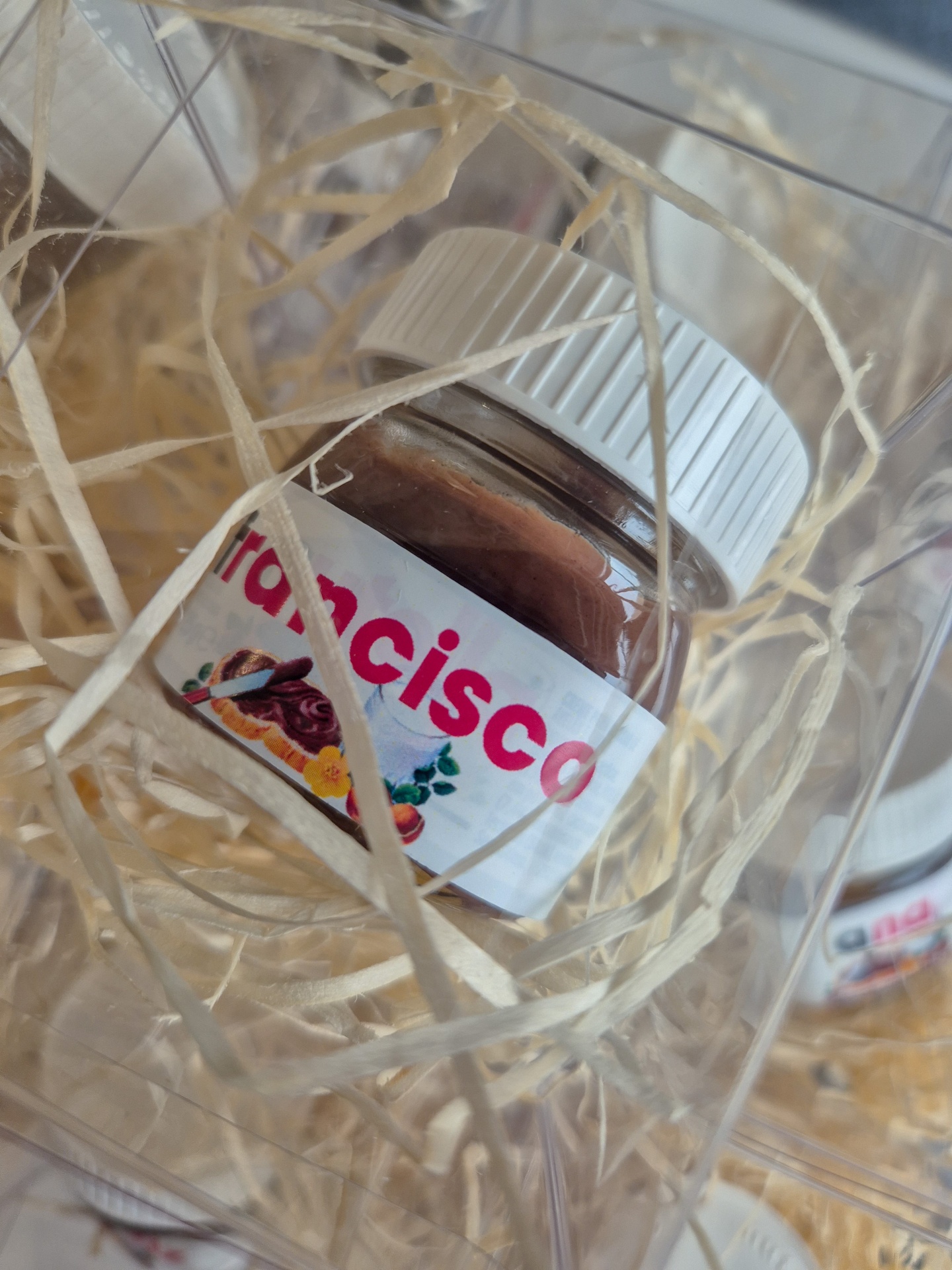 Frasco pequeno com creme marrom e rótulo 'Francisco' em embalagem transparente com palha