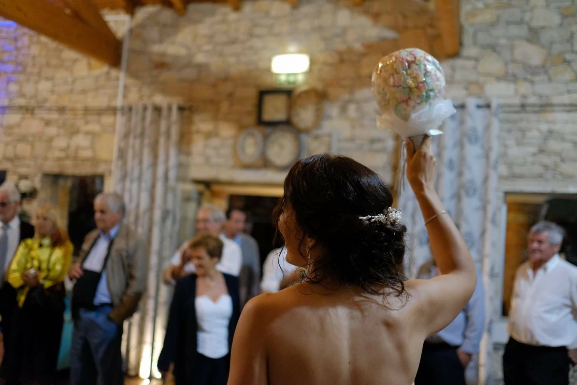Mulher de costas com vestido sem alças segurando bouquet colorido em ambiente interior rústico