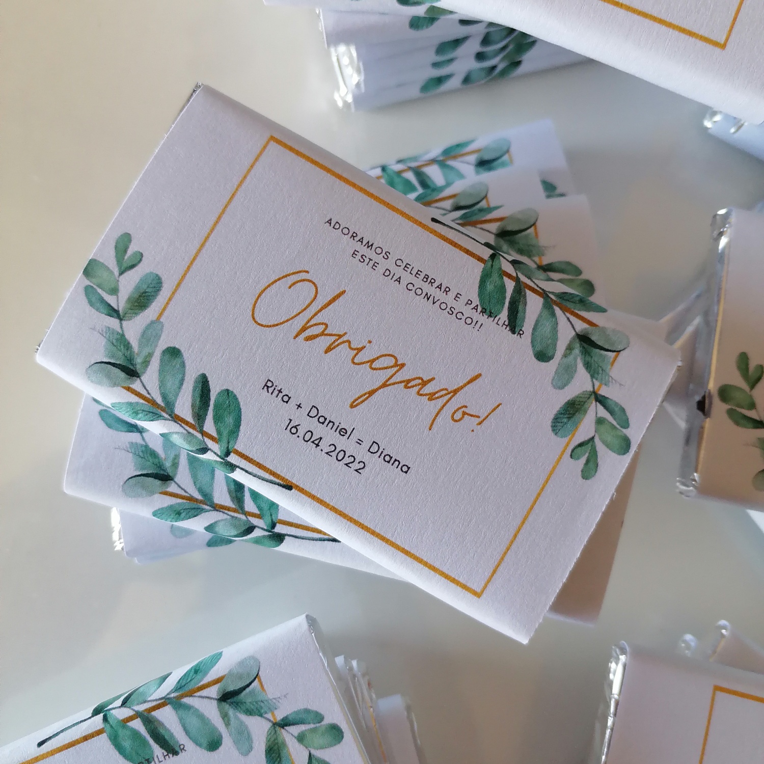 Pacotes de chocolates personalizados com etiqueta branca estampada com ramos verdes e texto em português