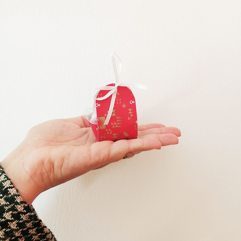 Caixa de presente vermelha com árvores douradas e fita branca na mão