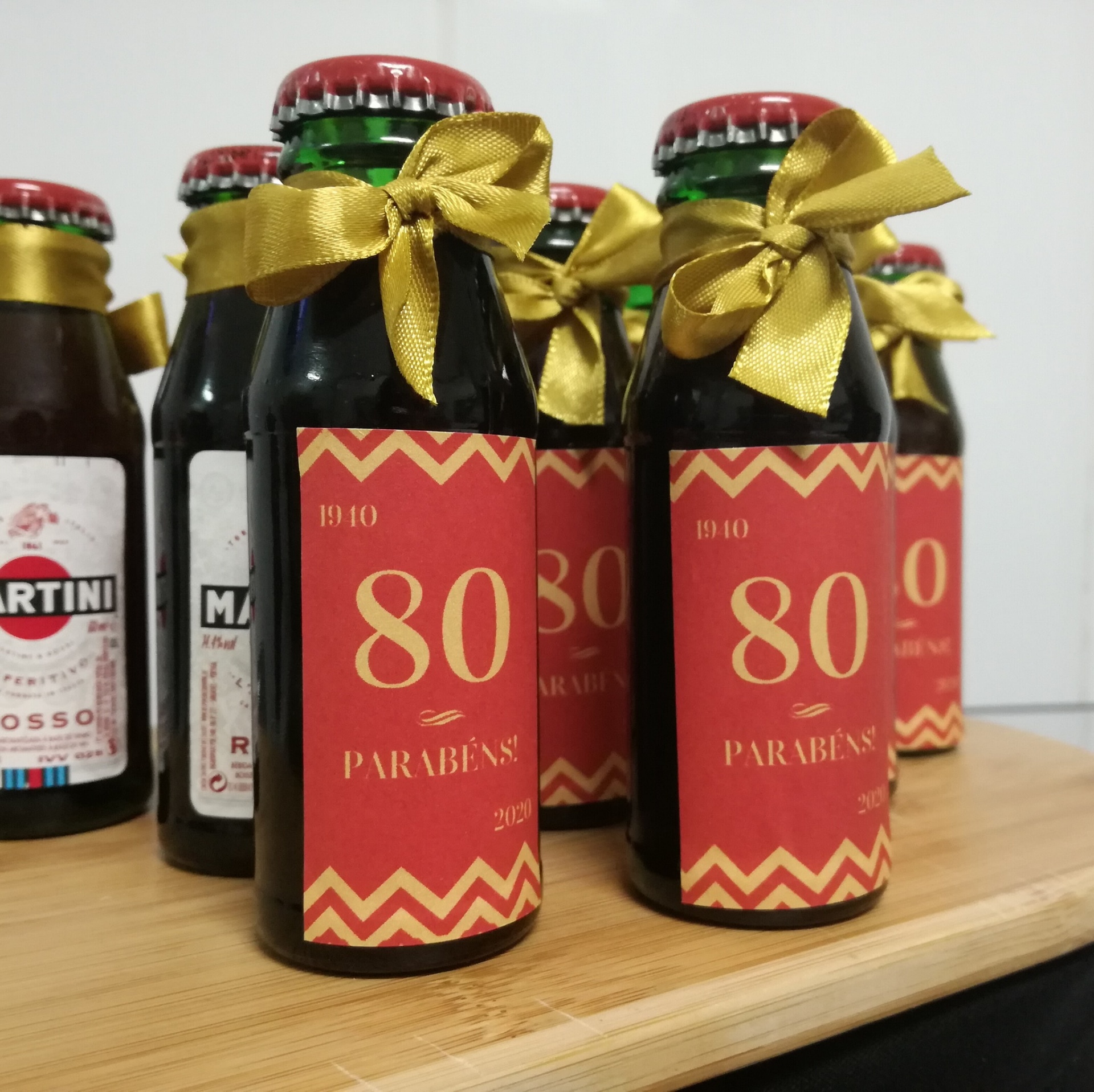Garrafas decoradas com rótulo 80 PARABÉNS e fita dourada em superfície de madeira
