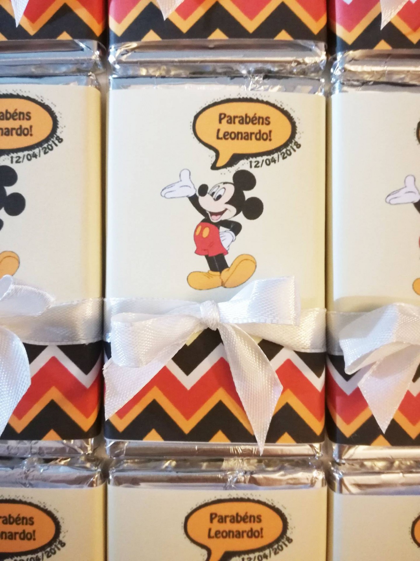 Chocolate com embalagem do Mickey Mouse com texto de parabéns e laço branco.