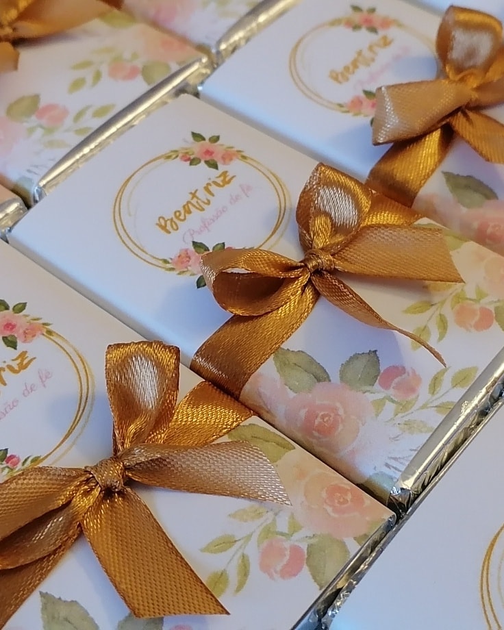 Chocolates embrulhados com papel branco floral e laços dourados