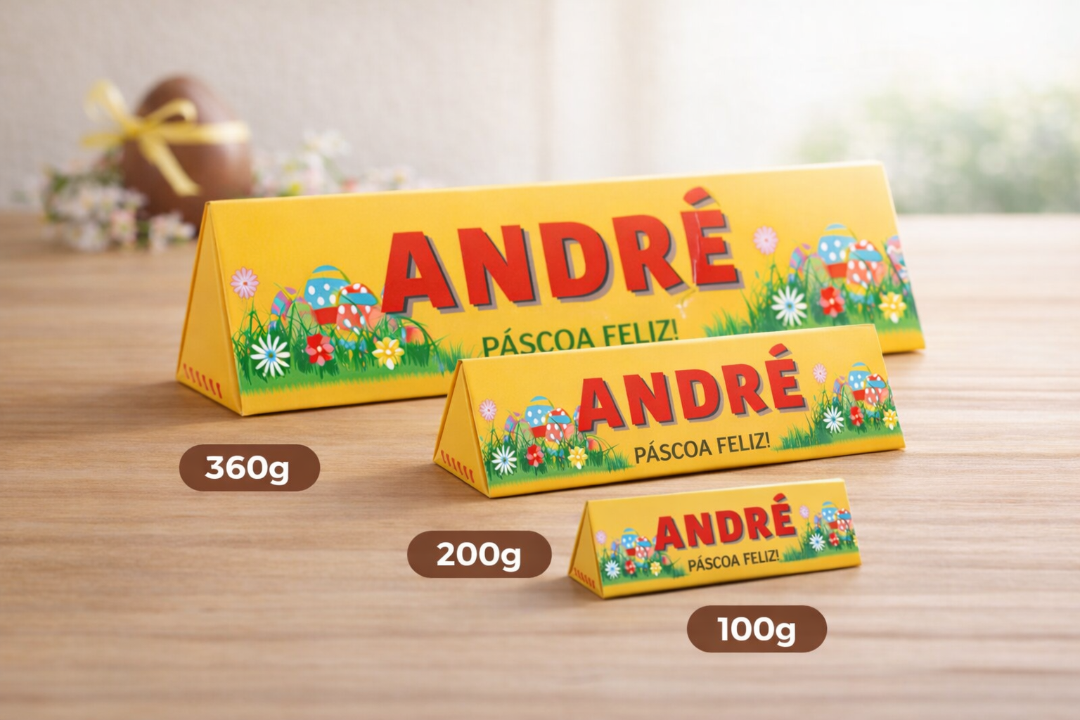 Três caixas triangulares amarelas com design de Páscoa e texto André Páscoa Feliz em diferentes tamanhos e pesos sobre mesa de madeira.