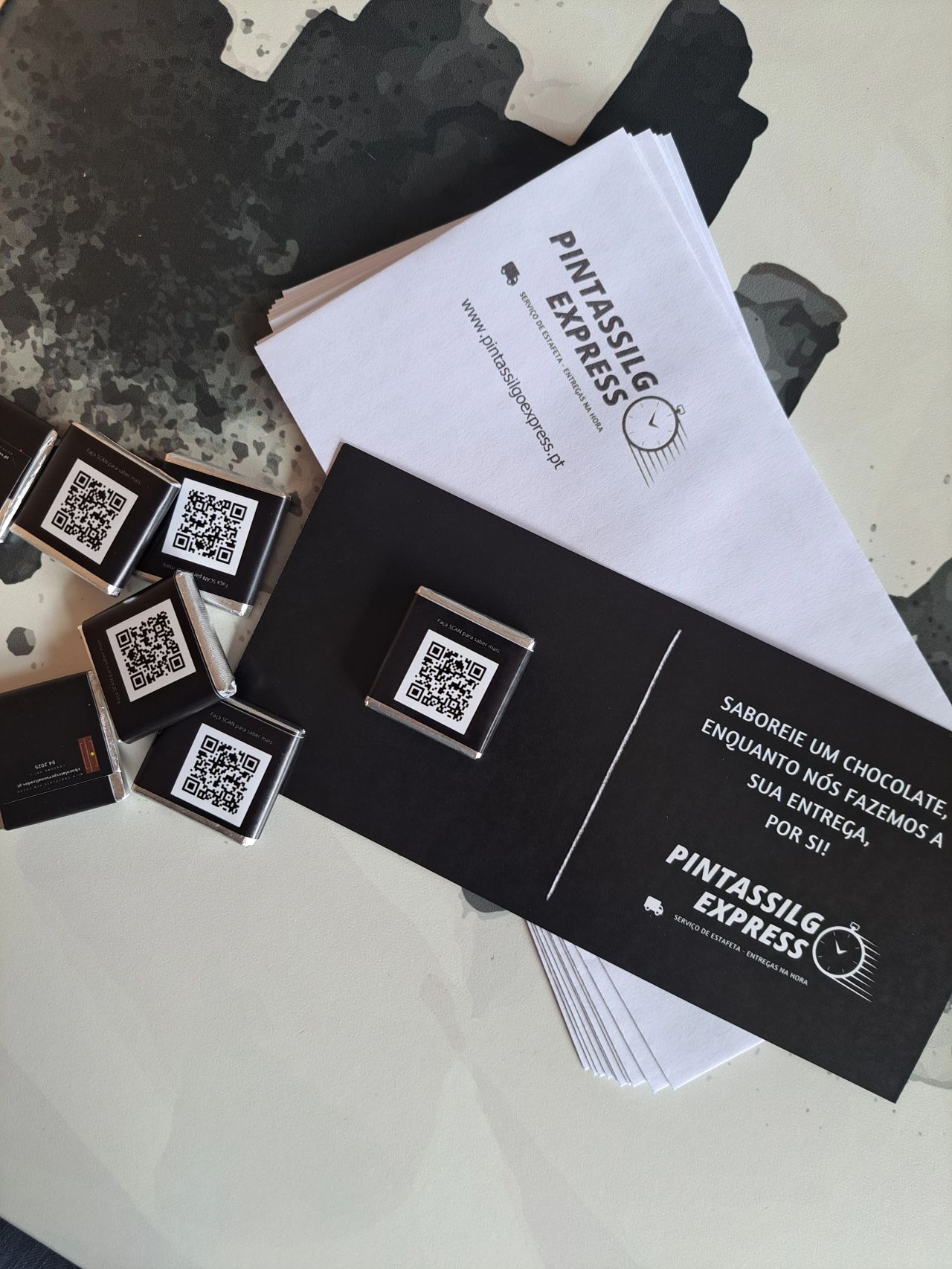 Chocolates pequenos com etiquetas QR e folheto promocional da Pintassilg Express