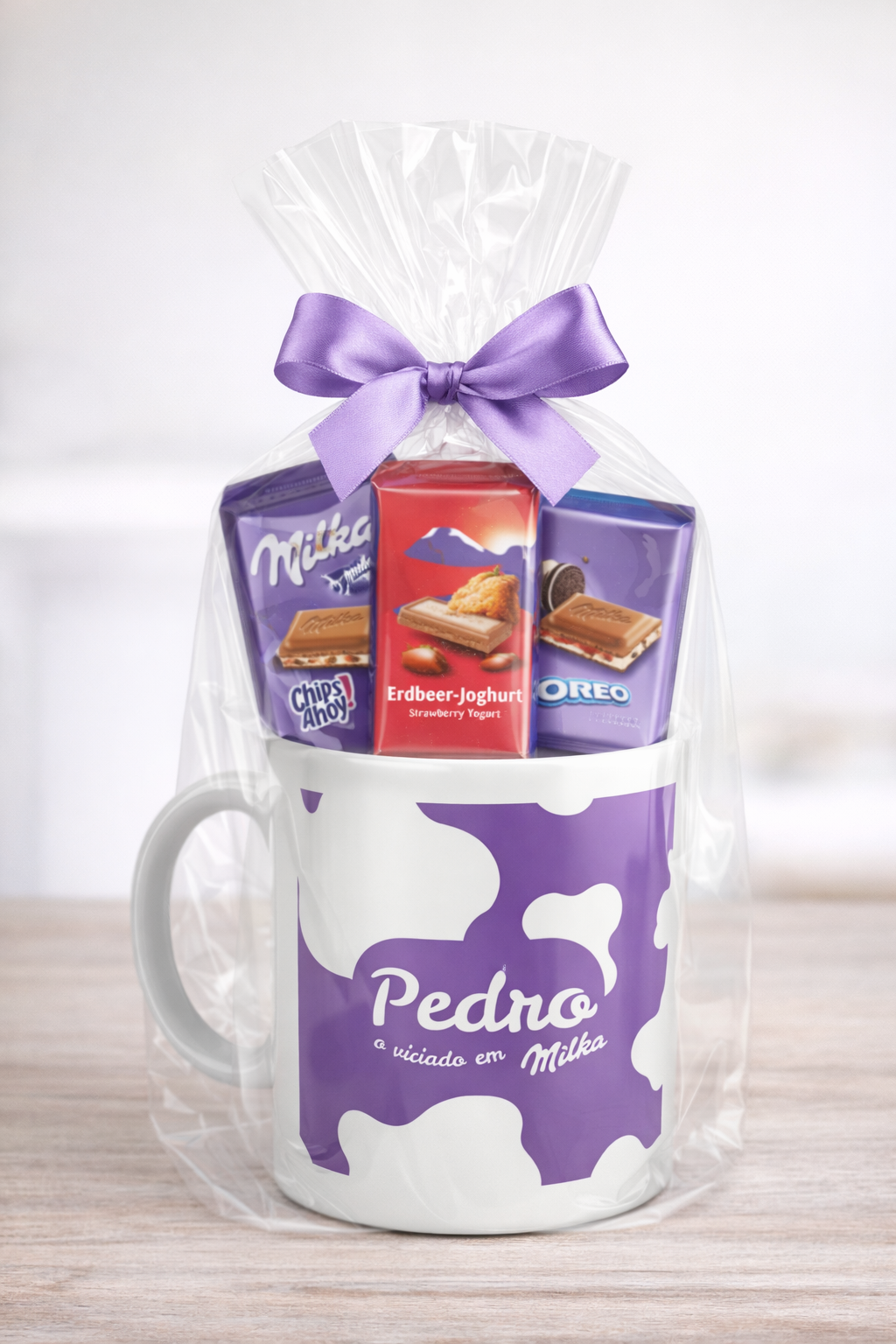 Caneca branca com manchas roxas e chocolates Milka embalada com fita roxa.