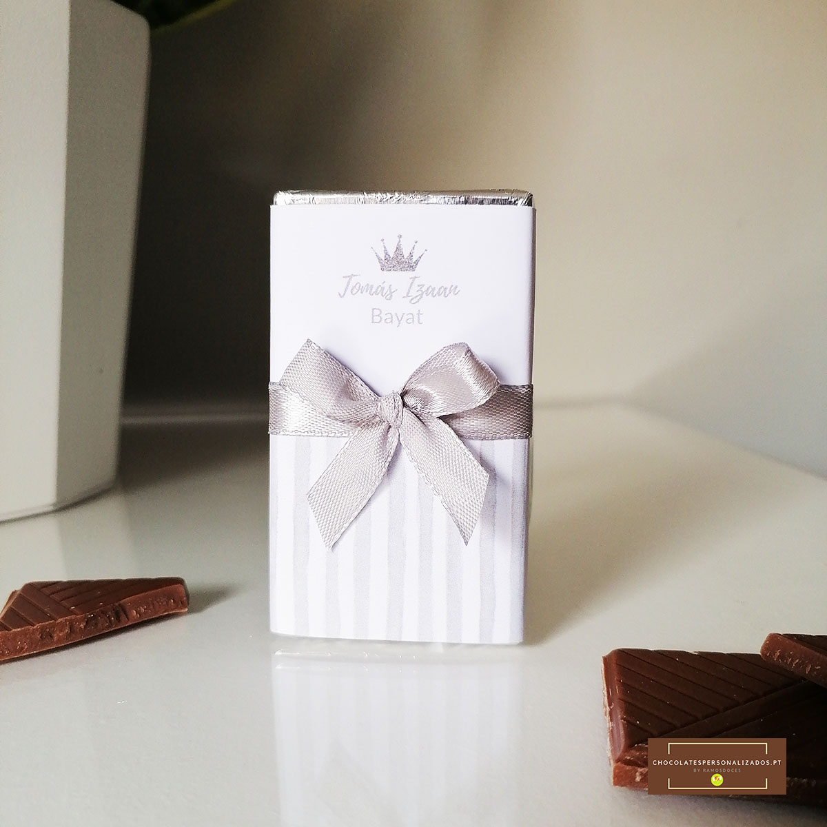 Embalagem branca com laço prateado e pedaços de chocolate ao leite.