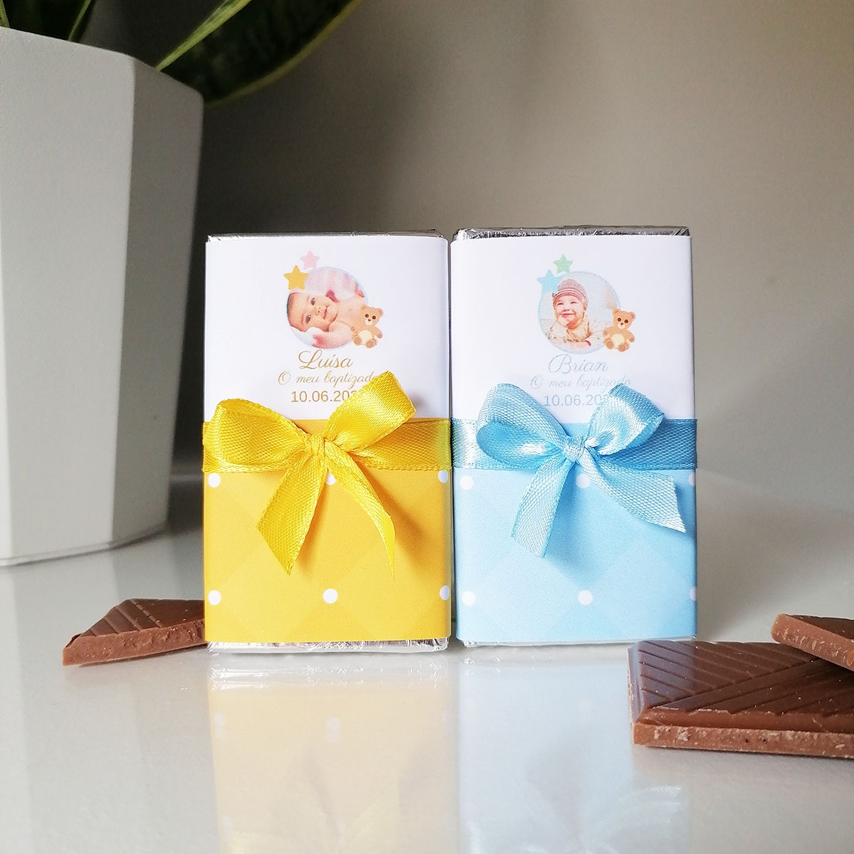 Dois chocolates embrulhados com laços coloridos e imagens de bebés numa superfície branca.
