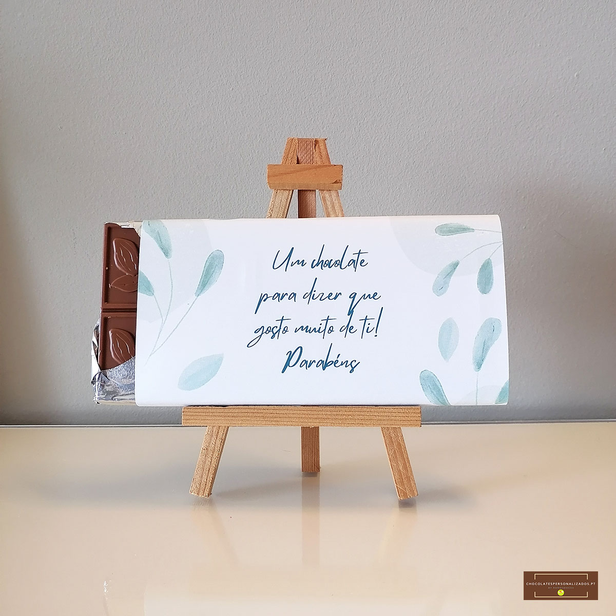Barra de chocolate embrulhada com mensagem em papel branco com folhas verdes num cavalete de madeira